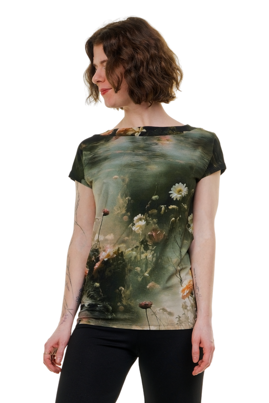 Detailansicht des Pixie Shirts Teichrose mit kurzem Arm, getragen von einem Modell in einem Zen-Garten. Das Shirt besticht durch einen künstlerischen Druck mit Wasserpflanzen und Teichrosen auf grünem Grund und wird in Berlin produziert.