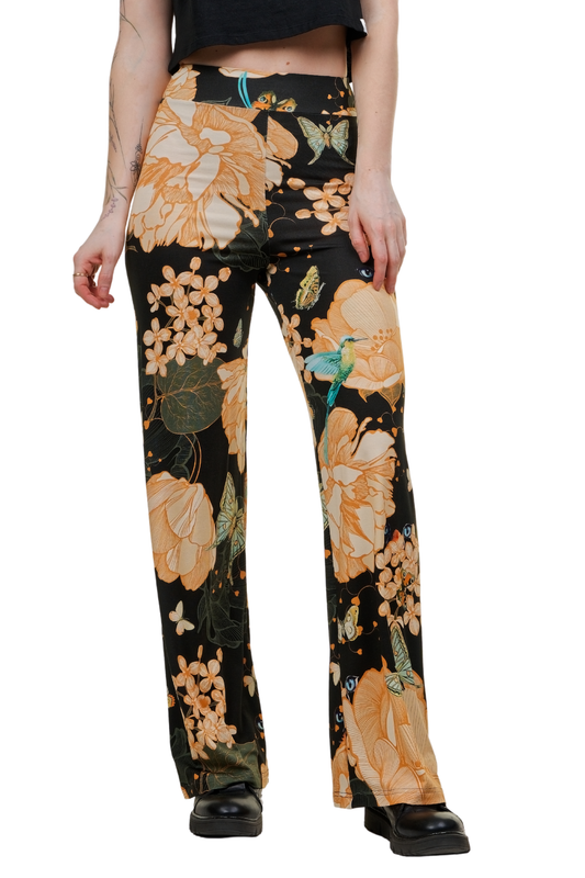 Frau trägt die weite Marlene-Hose 'Aura Gold' mit exotischem Muster aus goldenen Blüten und Kolibris auf schwarzem Grund, kombiniert mit einem schwarzen Crop-Top
