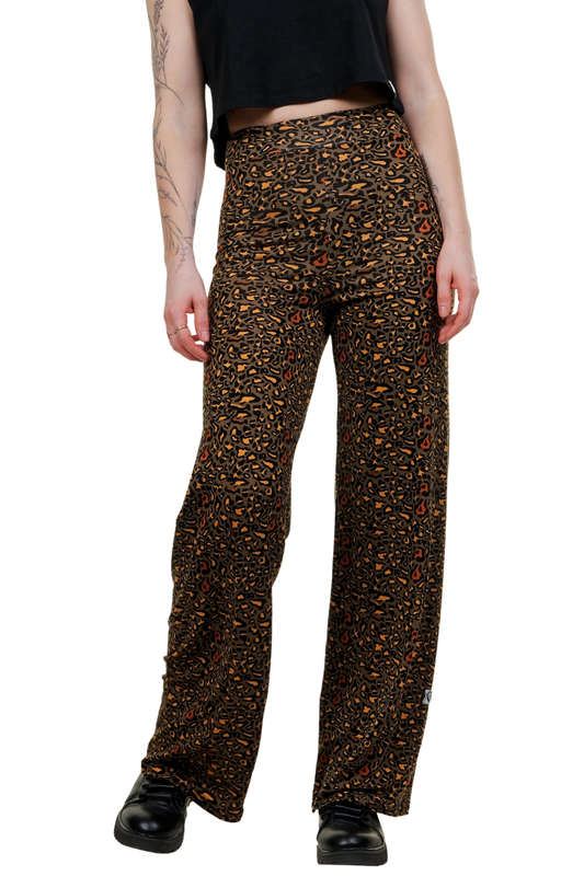 Frau trägt die weite Marlene-Hose 'Berlin Wildcat' mit klassischem Leopardenmuster in Braun und Orange, kombiniert mit einem schwarzen Crop-Top und schwarzen Boots